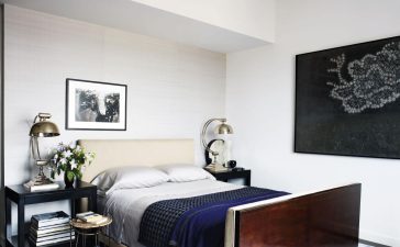 a wall of the master bedroom is covered in a silk by mdc wallcoverings and the bed bedding bedside tables and rug are by calvin klein home the side table and lamps are vintage and the painting is by carlos vega