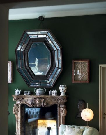 a fireplace in a room with tufted leather sofa and art deco mirror over the mantel filled with objects