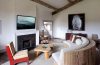 a seating area in a bedroom with a fireplace and curved sofa and red chair and large owl painting along the back wall