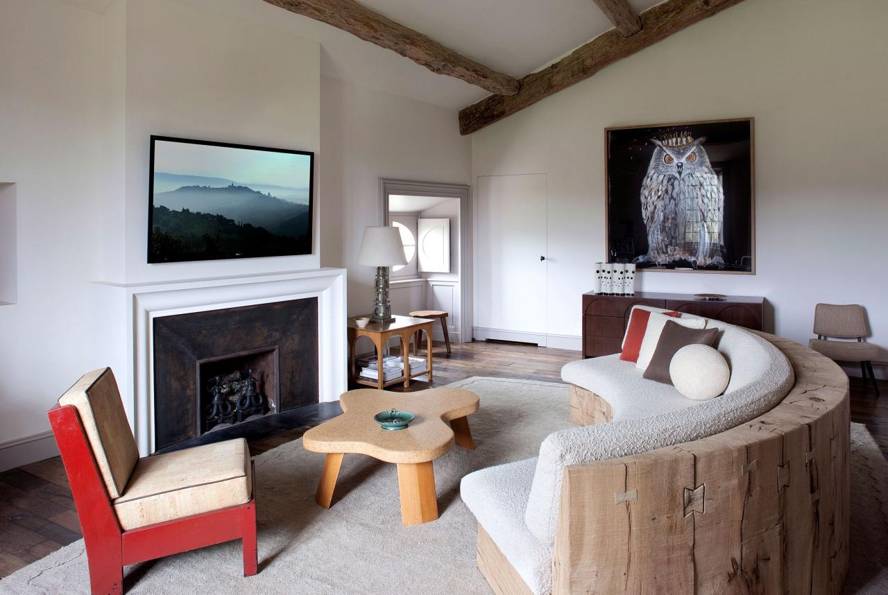 a seating area in a bedroom with a fireplace and curved sofa and red chair and large owl painting along the back wall