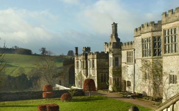 a large english manor building made of stone with a extensive lawn in front of it