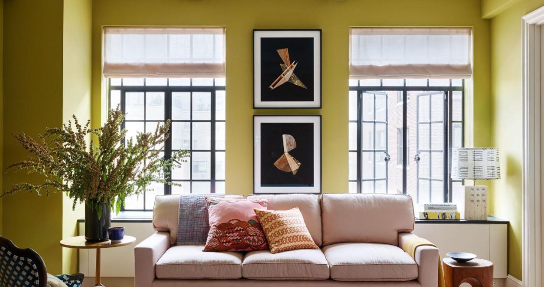 a living room with a pink sofa and a coloful glass coffee table and a blue and white armchair and tall french doors at the back and chartreuse painted walls