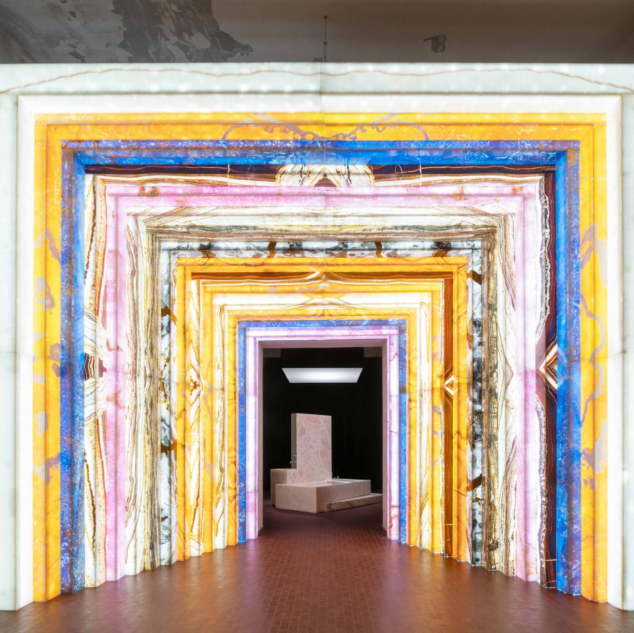 an archway made of colorful stone that leads to a pink marble bathtub installation